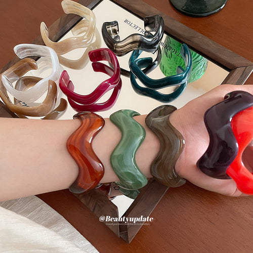 several wavy open resin cuff colors stacked around one wrist