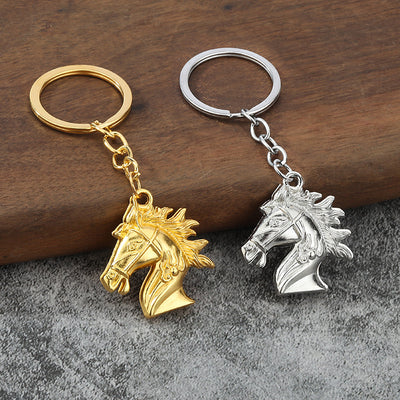 Gold-tone and silver-tone horse head keychains displayed together on wood and gray fabric.