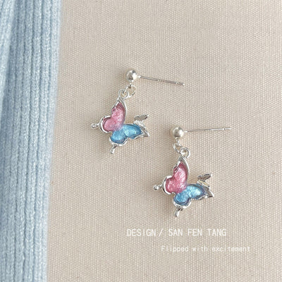 Silver ball studs with pink blue butterfly drops on beige fabric