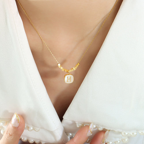 Model wearing white shell letter H pendant with gold tube beads