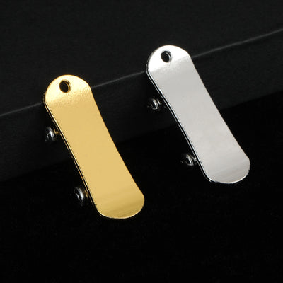 Gold-tone and silver-tone mini scooter deck charms leaning against a dark box