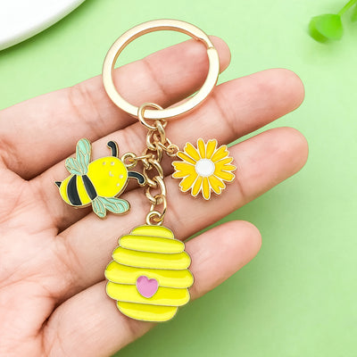 Image 1 showing a hand holding a yellow keychain with a bee and flower.
