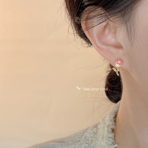 Gold-tone pink-edged white-rose green-leaf studs shown worn on an ear.