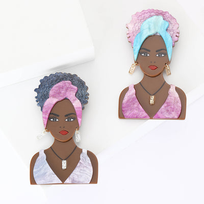 Front view of the acrylic woman portrait brooch in two headwrap colors on a white background