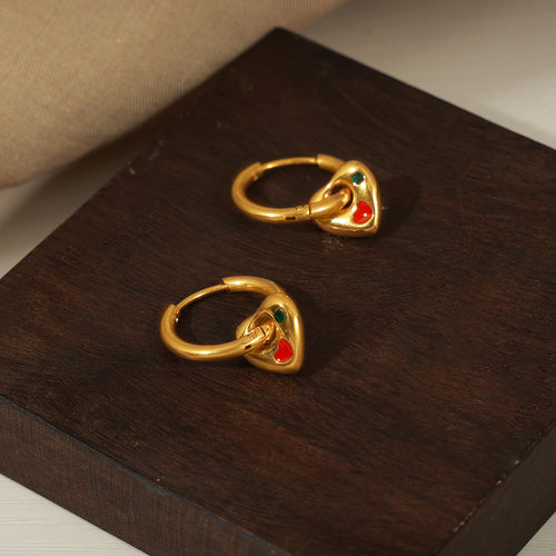 Pair of gold heart-charm huggie hoops on dark wood block