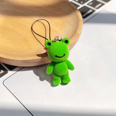 Green flocked frog phone strap charm standing on white surface by wooden dish
