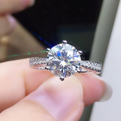 Six prong round clear center ring held between fingertips