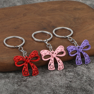 Three bow keychains in red, pink, and purple rest on a wooden block.