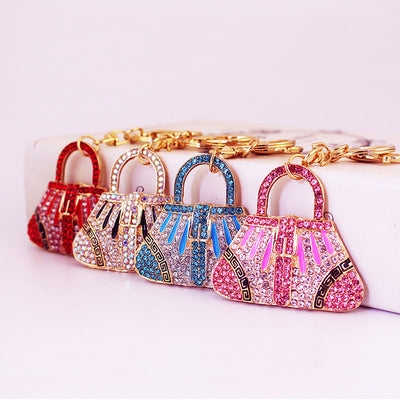 Four handbag-shaped keychains in red, white, blue, and pink arranged in a row.