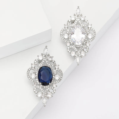 Two silver filigree brooches with clear and blue oval centers on white blocks