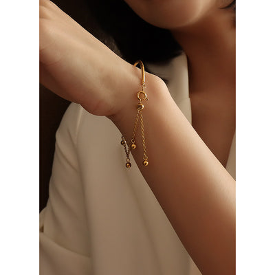 Model wrist wearing gold open bar cuff ball tassel bracelet