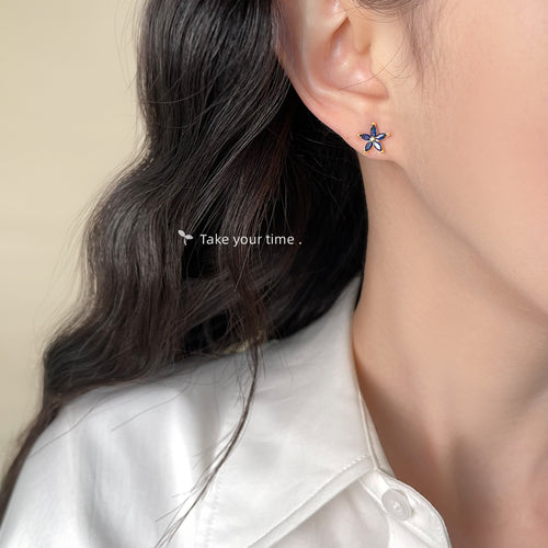 Blue flower stud worn on ear with white collared shirt