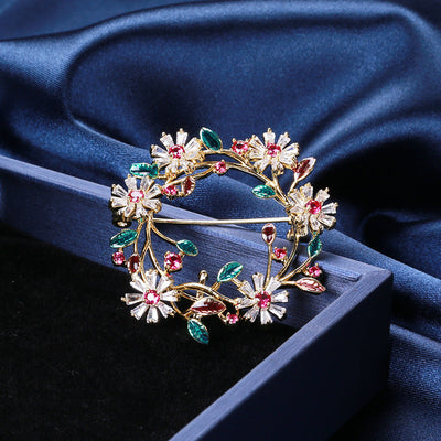 Front view of floral crystal wreath brooch with green and burgundy leaves against a white background.
