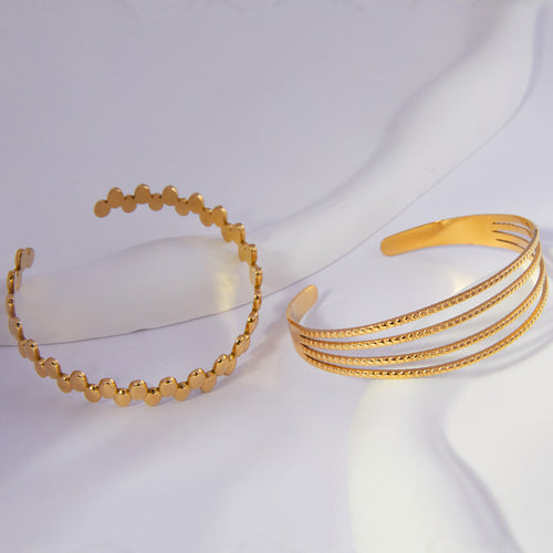 Two gold open cuffs side by side on white curved prop