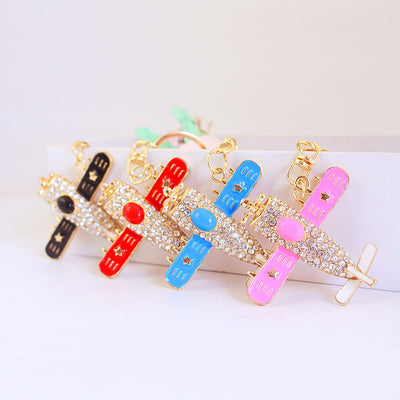 Four gold-tone airplane keychains in black, red, blue, and pink are arranged together.