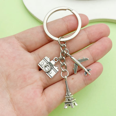 A silver-tone Eiffel Tower, camera and airplane keychain held in a hand.