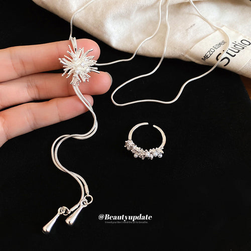 Silver starburst necklace and open ring held against black fabric