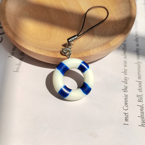 Blue and white resin lifebuoy phone charm with black strap on wood dish