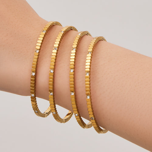 Four gold gear bangles worn stacked on wrist