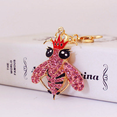 Close-up of a pink rhinestone bee wearing a red crown and black enamel eyes.