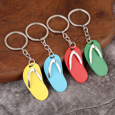 Four flip flop keychains in yellow, sky blue, red, and green displayed on a wood surface.