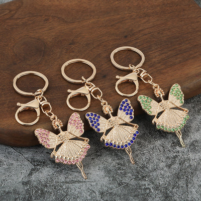 Three gold-tone winged girl charms with pink, blue, and green stones rest on a wooden surface.