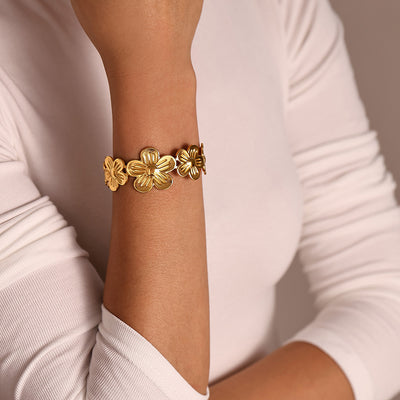 Gold five-petal flower open cuff on wrist over white sleeve