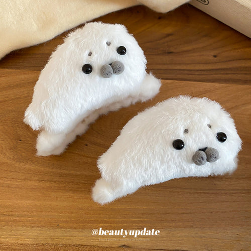 Two white plush seal face hair claws on wooden table