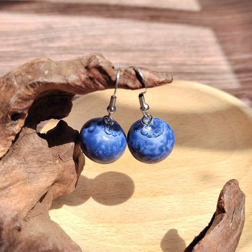 Blue resin blueberry dangle earrings hanging near driftwood on wooden dish