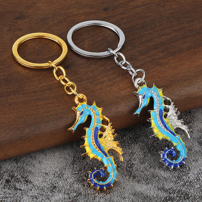 Gold-tone and silver-tone seahorse keychains displayed together on wood and gray fabric.