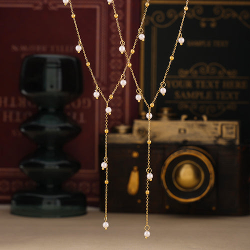 Two gold pearl Y lariats hanging before books and camera