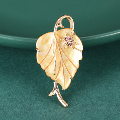 Gold shell leaf brooch with pink ladybug on green fabric