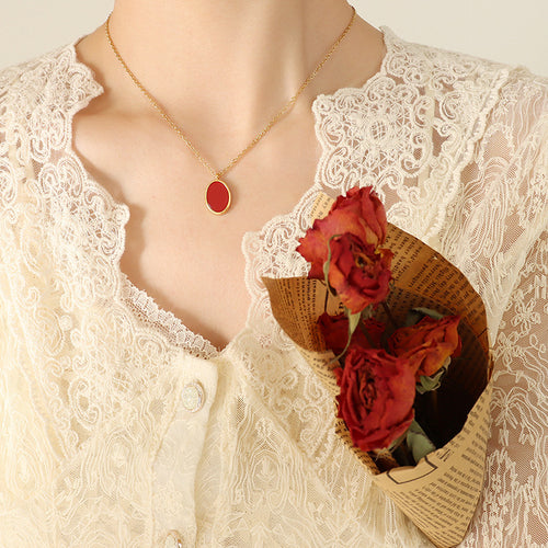 Gold red oval pendant necklace worn with lace blouse and dried rose bouquet