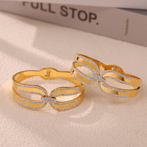Two gold bow crystal bangles on sand with books in background