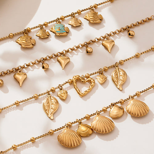 Close flat lay of gold fish shell leaf and heart charm bracelet chains