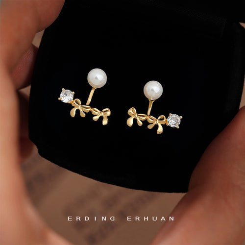 Gold pearl bow crystal ear jackets held above black jewelry tray