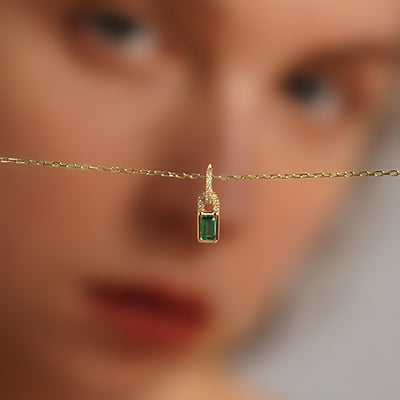 Gold green rectangle pendant necklace held in front of face