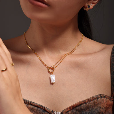 Model wearing gold dual-chain necklace with rectangular white pearl pendant at collarbone
