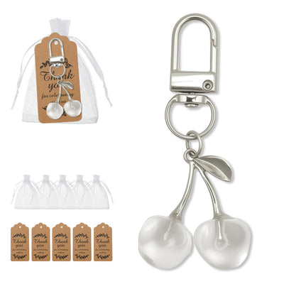 A white double-cherry keychain is displayed beside white organza bags and brown printed tags.