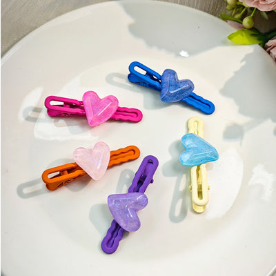 Five glitter heart duck bill hair clips in mixed colors on white plate