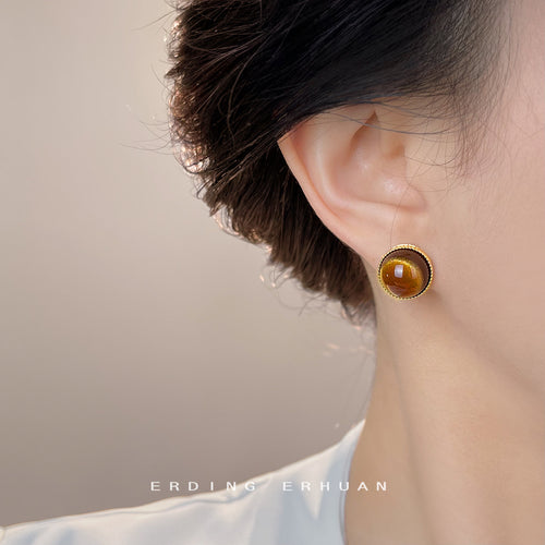 Model wearing round gold tiger eye cabochon stud on ear