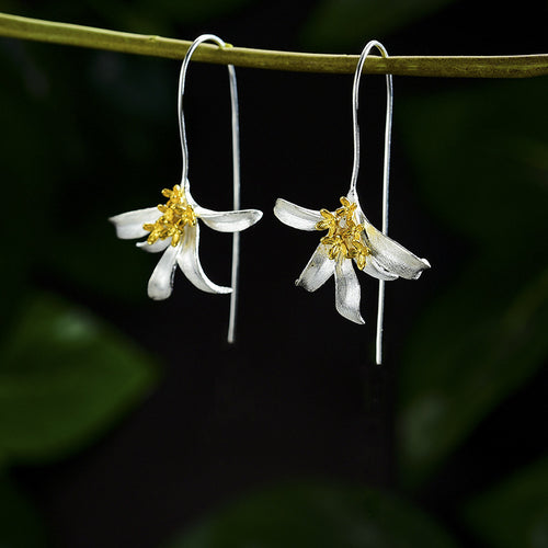 Two-tone lily flower earrings hanging from green branch