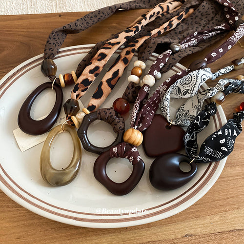 fabric cord necklaces with large geometric resin pendants shown in an on-ear styling view