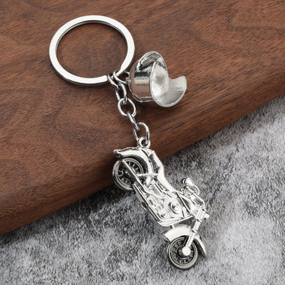 Close view of a silver-tone motorcycle pendant and helmet charm on wood.
