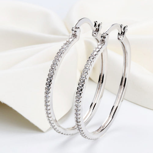 Pair of white metal pavé clear stone hoop earrings on white fabric