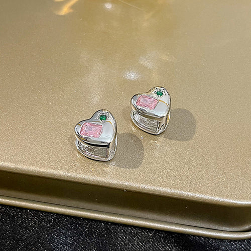 Silver heart pink stone huggies on gold metallic tray surface