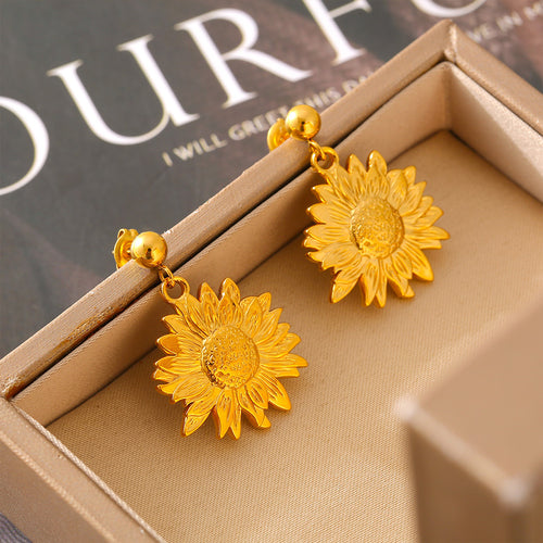 Gold sunflower drop earrings in beige jewelry box on magazine