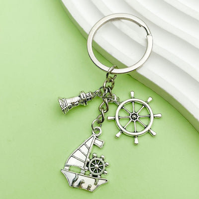 Silver-tone keyring with lighthouse, ship wheel, and sailboat charms on a green background.