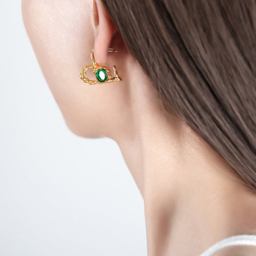 Model wearing gold asymmetric heart earring with green oval stone