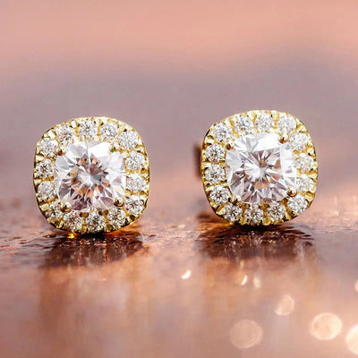 Yellow gold cushion halo clear stud earrings pair on reflective copper surface